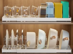 Expandable white pot and pan organizer rack neatly storing frying pans, pot lids, cutting boards, and bakeware inside a modern kitchen cabinet.