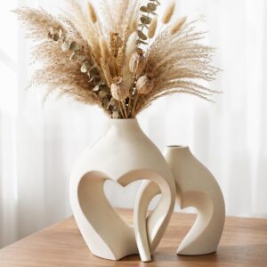 Set of two white ceramic heart-shaped vases with dried pampas grass on a modern wooden table in a cozy living room.
