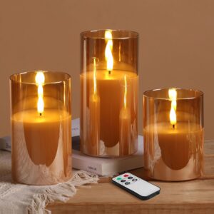 Set of three gold glass flameless LED candles with realistic flickering flames and remote control displayed on a modern wooden coffee table.