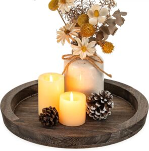 Round rustic wooden decorative tray on a coffee table styled with flameless candles, ceramic vase, and seasonal home décor.